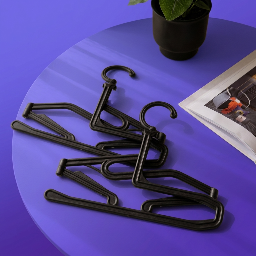Cintres pliables PlyoFold noirs repliés à plat et empilés sur une table, à côté d'un magazine ouvert